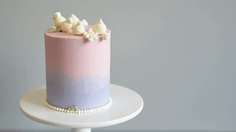 A dainty 4-inch bento cake with pastel gradient frosting, adorned with white buttercream flowers, presented on a minimalist ceramic stand against a light gray background.