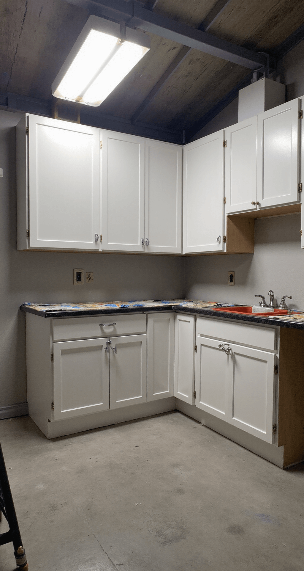 Professional painter's workspace in a 16x18ft kitchen, featuring drop cloths for surface protection, organized tools on a workbench, labeled cabinet doors, and bright overhead lights illuminating a systematic and clean setup.
